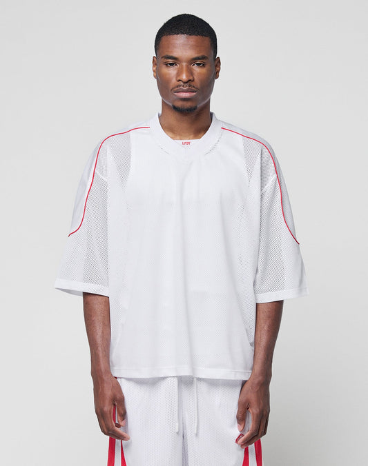 A man faces forward in a LIVE FAST DIE YOUNG Basic Mesh Jersey and matching 100% polyester white mesh shorts with red accents, both in an oversize fit, against a plain light gray background. | model