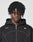 A person with medium-dark skin and tightly coiled hair looks at the camera, wearing the LIVE FAST DIE YOUNG LFDY Active Fleece Hooded Zip—an oversize black hoodie with a white logo on the chest—against a plain light background.