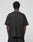 A person with short curly hair stands with their back to the camera, wearing the LIVE FAST DIE YOUNG Live Fast LF Tee in black and matching black pants against a plain light gray background.