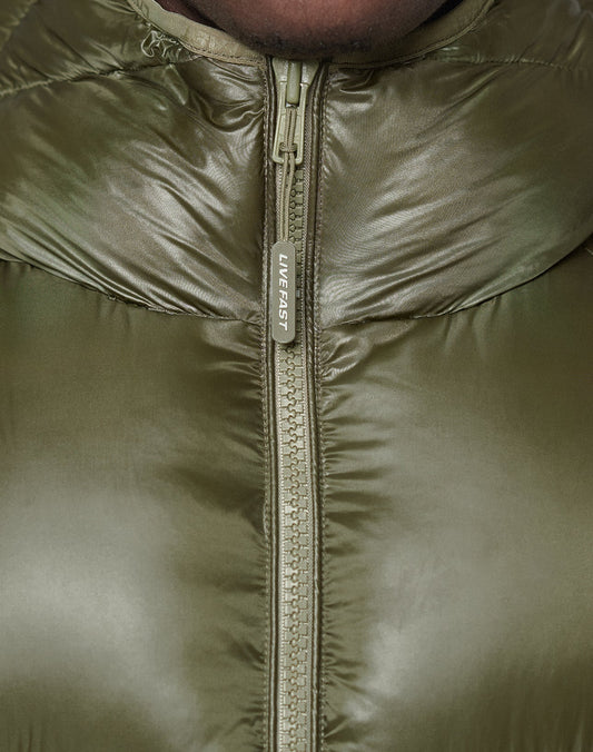 Close-up of the olive green Live Fast Puffer Jacket by LIVE FAST DIE YOUNG, fully zipped to the top. The zipper pull features "LIVE FAST" in white and the jacket is crafted from durable Nylon Obermaterial.