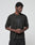 A person wears the Live Fast LF Tee by LIVE FAST DIE YOUNG, a black oversized t-shirt with a geometric logo and "LIVEFAST" front print. They stand against a light background, looking to the side with hands clasped.