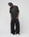 Someone stands against a plain light background wearing the black LIVE FAST DIE YOUNG Live Fast LF Tee (oversize fit, front print), loose black cargo pants, white sneakers, and a patterned black headwrap while looking down.