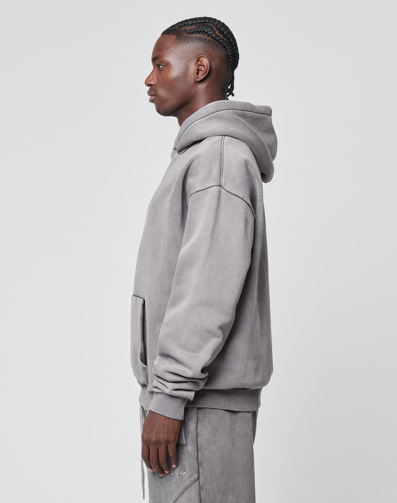 A man stands in profile against a plain background, wearing the LIVE FAST DIE YOUNG Basic Blank Hooded in gray with matching pants. His neat cornrows elevate the casual look, crafted from soft Baumwolle.