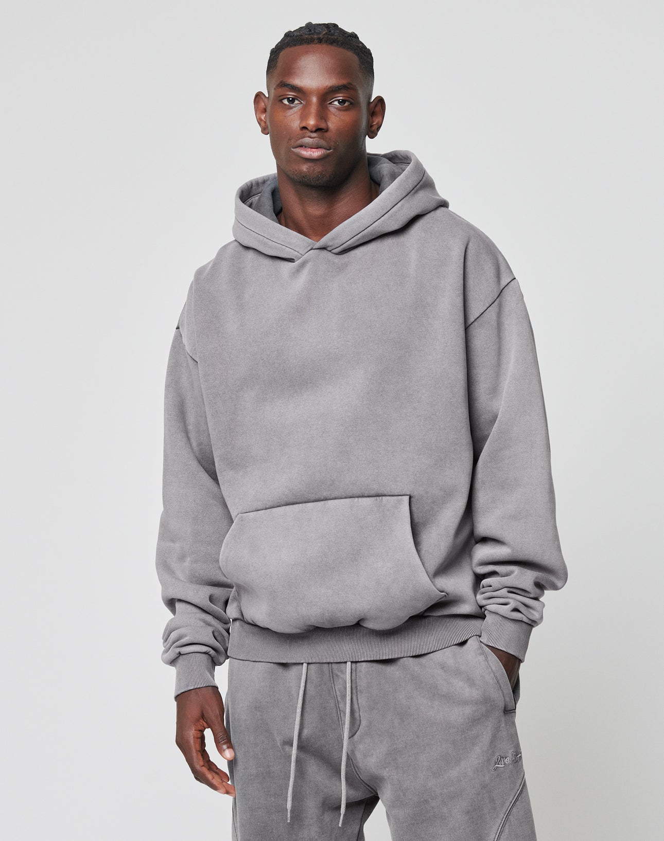 A man in a grey Basic Blank Hooded sweatshirt by LIVE FAST DIE YOUNG and matching sweatpants stands against a plain light background, facing the camera with a neutral expression.