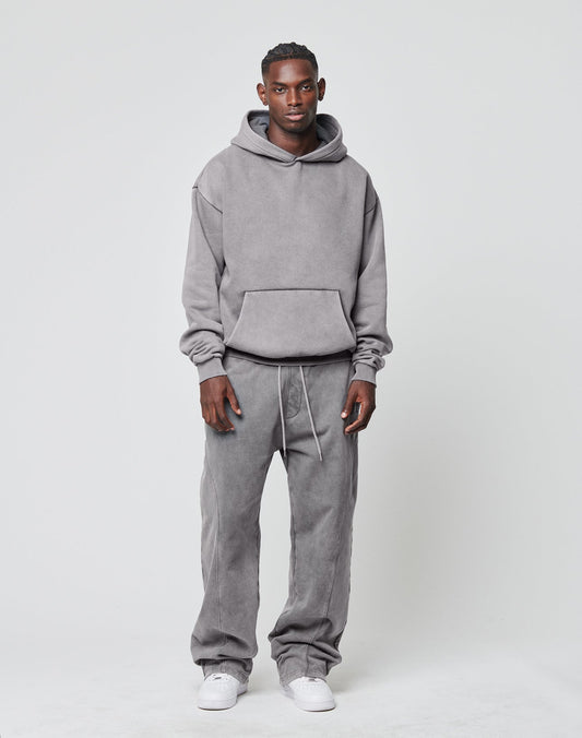 A man stands against a light background, facing forward with a neutral expression. He wears the LIVE FAST DIE YOUNG Basic Blank Hooded in gray, matching gray drawstring sweatpants, and white sneakers.