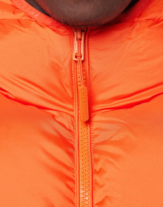Close-up of the bright orange Live Fast Puffer Jacket by LIVE FAST DIE YOUNG, featuring a smooth, slightly glossy wasserabweisend fabric and a matching zipper partially pulled up. The EVERREST zipper pull is visible below part of the wearer’s face.
