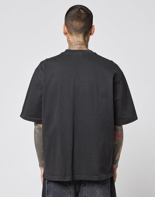 A person with short hair and visible tattoos stands with their back to the camera, wearing a plain black LIVE FAST DIE YOUNG LFDY Europe Run Tee and dark denim shorts against a neutral background.