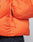 A close-up of the LIVE FAST DIE YOUNG Live Fast Puffer Jacket in orange with water-repellent material, visible zipper pull, and part of a sleeve; the person pairs it with dark pants.
