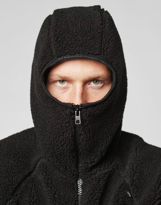 A person in a LIVE FAST DIE YOUNG Live Fast Teddy Jacket, with hood zipped to show just their eyes, nose, and forehead, stands against a plain light grey background. Subtle embossed branding adds a refined touch.
