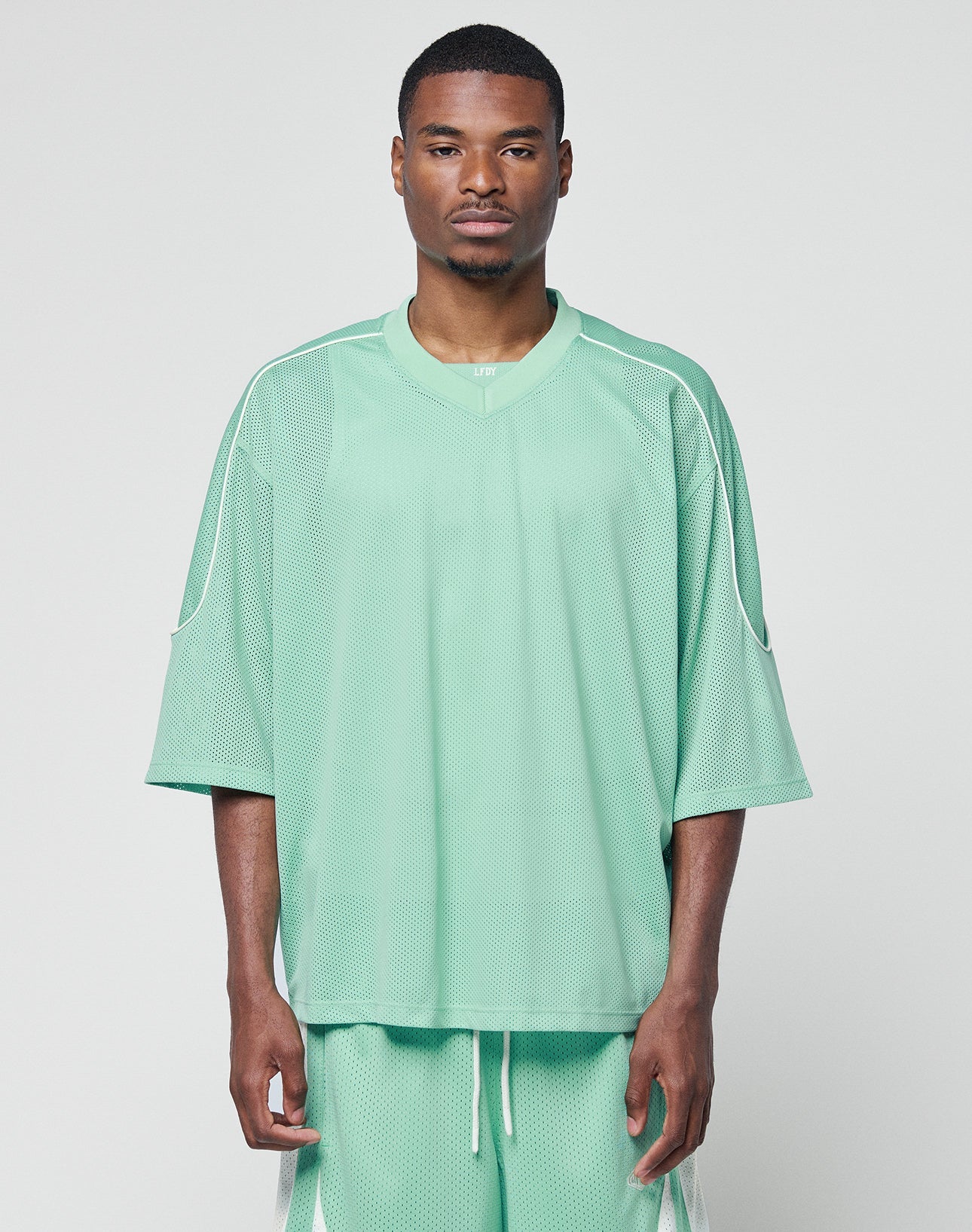 A man wearing the LIVE FAST DIE YOUNG Basic Mesh Jersey and matching mint green shorts with contrast piping stands against a white background, looking directly at the camera with a neutral expression.