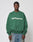 A man in a green LIVE FAST DIE YOUNG LFDY Europe Run Sweater with LIVE FAST EUROPEAN on the front stands facing forward. Made from soft Baumwolle, he pairs it with blue jeans against a light gray background.