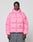 Wearing the LIVE FAST DIE YOUNG Live Fast Puffer Jacket in oversize bright pink nylon with hood and reflective shark logo print, a person with braided hair and loose gray pants stands against a light gray background.