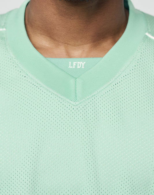 Close-up of a person wearing the Basic Mesh Jersey by LIVE FAST DIE YOUNG. This light green, 100% polyester mesh top features LFDY branding on the collar and showcases its oversized fit around the neckline and upper chest.