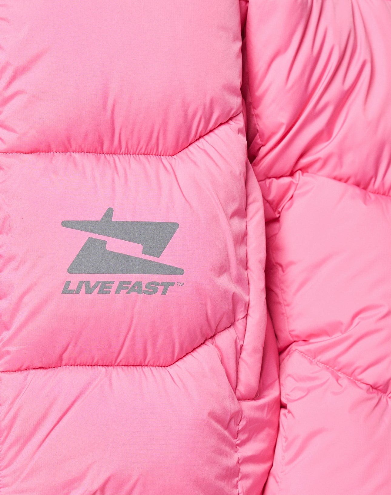 Close-up of the Live Fast Puffer Jacket by LIVE FAST DIE YOUNG in oversize fit, with a pink nylon quilted design, grey graphic logo, and "LIVE FAST" in reflective print.