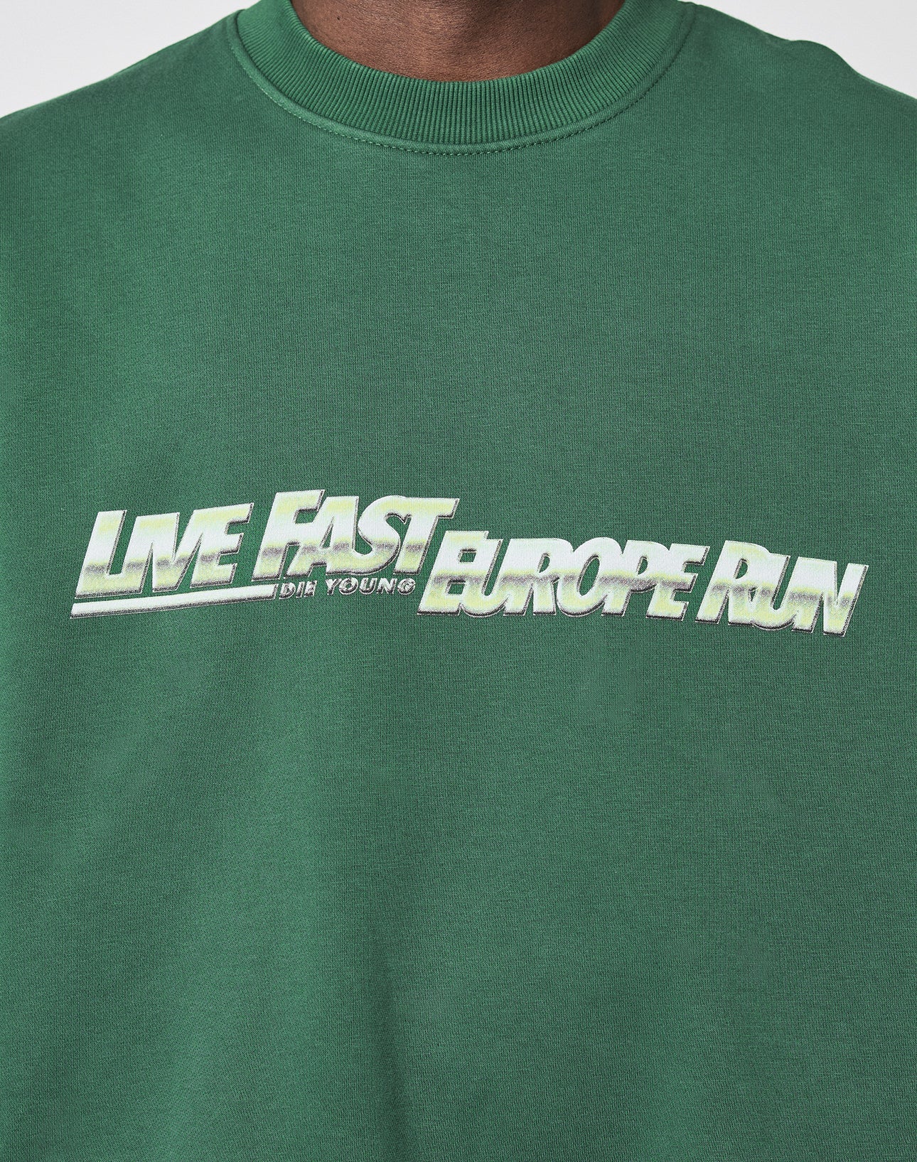 A person wears the LIVE FAST DIE YOUNG LFDY Europe Run Sweater, an oversize green sweatshirt with LIVE FAST EUROPE RUN printed in bold white and green gradient letters across the chest.