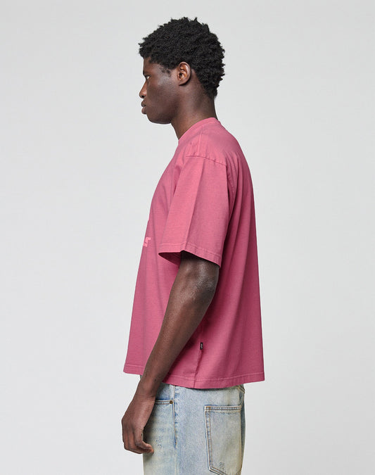 A man in profile faces left, wearing a LIVE FAST DIE YOUNG Live Fast LF Tee in mauve with an oversize fit and light blue jeans, standing against a plain light gray background.