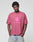 A person wearing the LIVE FAST DIE YOUNG Live Fast LF Tee, an oversized rose 100% Baumwolle T-shirt with bold LIVEFAST frontprint, stands with hands in pockets against a plain light background.