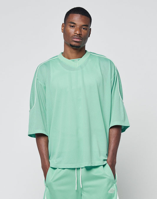 A man wearing the LIVE FAST DIE YOUNG Basic Mesh Jersey in mint green with contrast piping and matching shorts stands against a plain light gray background, hands in his pockets.