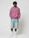 A person stands against a plain background wearing a pink LIVE FAST DIE YOUNG Live Fast Rivet Hooded Zip with handgefertigtem Sprayeffekt, light blue baggy denim shorts, white crew socks, and white sneakers.