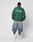 A person faces away, wearing the green LFDY Europe Run Sweater by LIVE FAST DIE YOUNG with back print, light blue knee-length denim shorts, white crew socks, and white sneakers, set against a plain white background.