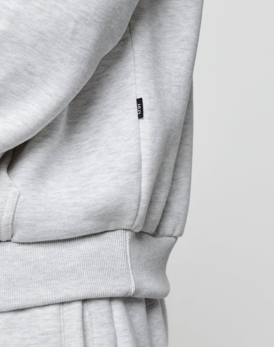 Close-up of the LIVE FAST DIE YOUNG Basic Blank Hooded in light grey, featuring an oversized fit, ribbed waistband, pocket, and a small black tag with white text. The soft cotton-polyester blend fabric and casual style are clearly visible.
