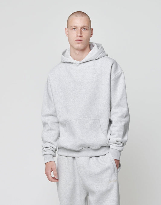 A person with short hair stands against a light background, wearing the LIVE FAST DIE YOUNG Basic Blank Hooded in an oversize fit and matching sweatpants made from soft Baumwolle, with one hand by their side and a neutral expression.