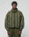 A man in the LIVE FAST DIE YOUNG LFDY Nylon Trackjacket, olive green with white vertical stripes and matching pants in Oversize Fit, stands against a light gray background, looking directly at the camera with a neutral expression.