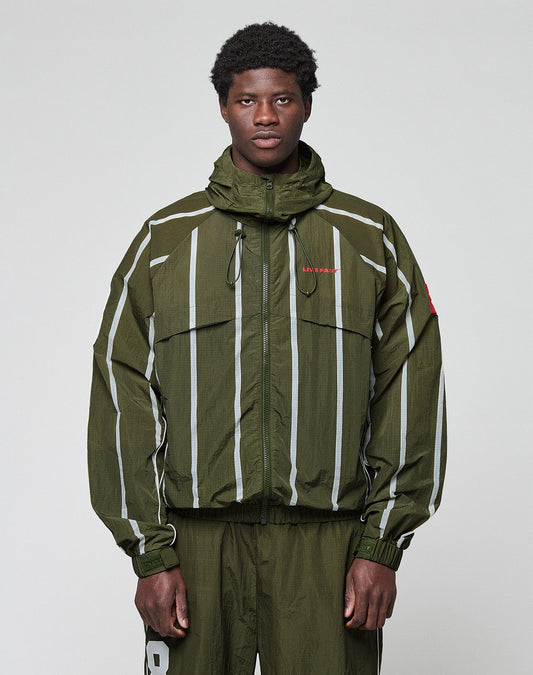 A man in the LIVE FAST DIE YOUNG LFDY Nylon Trackjacket, olive green with white vertical stripes and matching pants in Oversize Fit, stands against a light gray background, looking directly at the camera with a neutral expression.