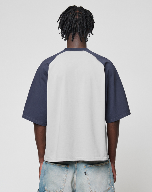 A person with short twisted hair is seen from the back, wearing the Live Fast Raglan Tee by LIVE FAST DIE YOUNG and light blue distressed jeans against a simple, light background.
