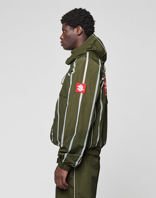 A person stands sideways wearing the LIVE FAST DIE YOUNG LFDY Nylon Trackjacket in green with a relaxed fit, white vertical stripes, hood with elastic drawstring, and bold red patches with white logos on the sleeve and back. Plain light gray background.