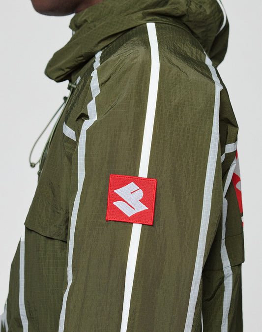 A person wears the LFDY Nylon Trackjacket by LIVE FAST DIE YOUNG—an olive green, oversize jacket with white vertical stripes, a red patch with a white geometric symbol on the sleeve, visible stitching, and a hood with elastic tunnelzug.