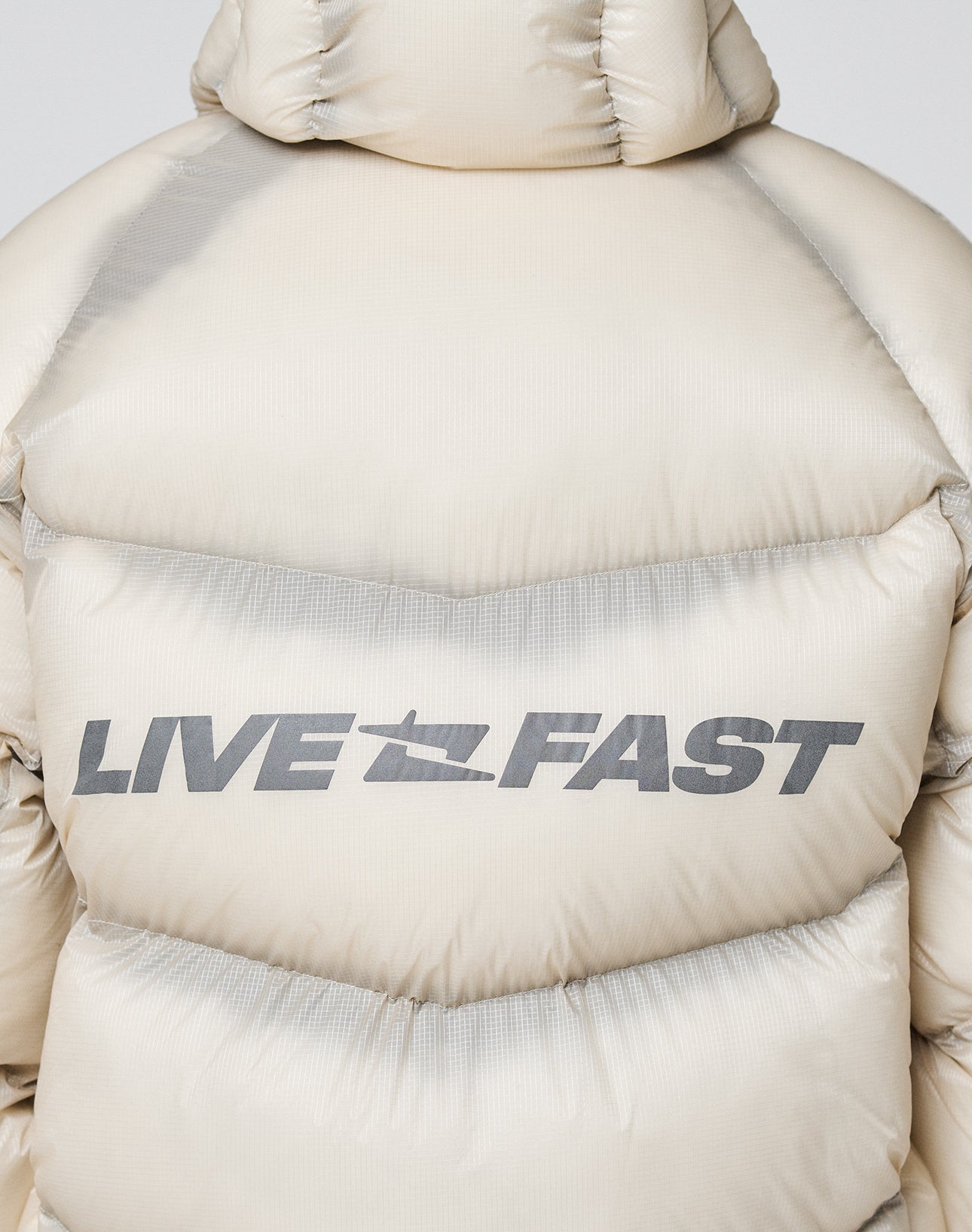 The Live Fast Puffer Jacket by LIVE FAST DIE YOUNG features bold, gray "LIVE FAST" lettering across the upper back, adding standout style to this beige oversized nylon jacket.