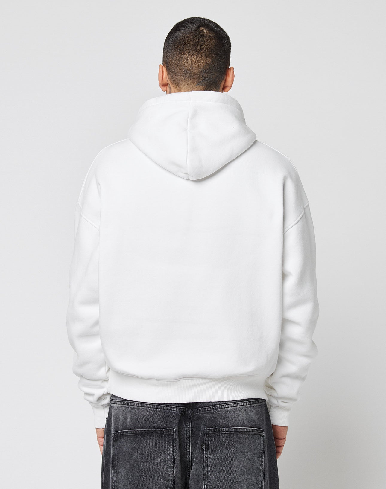 A person with short dark hair, seen from behind, wears a plain white Live Fast Europe Run Hooded by LIVE FAST DIE YOUNG and dark gray jeans against a plain light background.