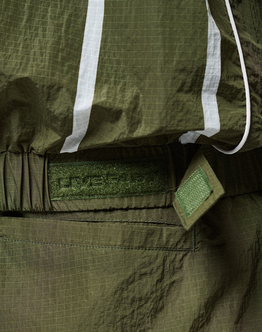 Close-up of an olive green LFDY Nylon Trackjacket by LIVE FAST DIE YOUNG, featuring crinkled fabric, white reflective stripes, Velcro strap, elastic hood drawstring, embossed patch detail, and an oversize fit for comfort.