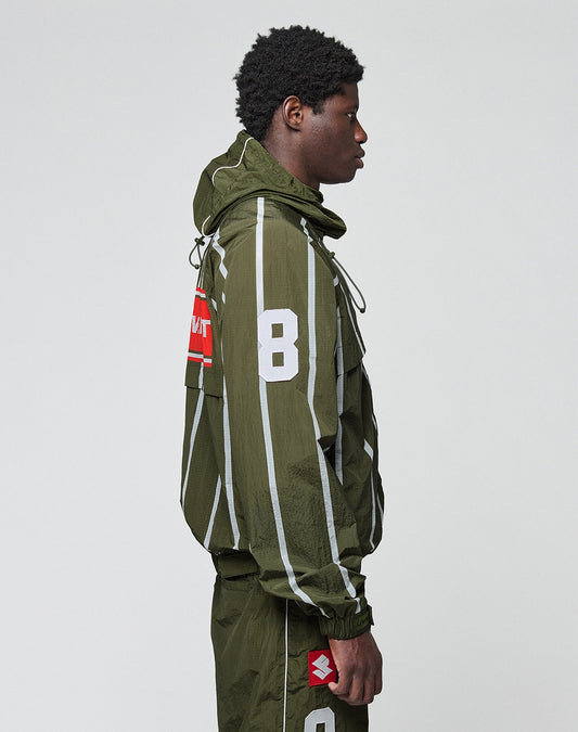 A person in profile wears an oversize fit olive LFDY Nylon Trackjacket by LIVE FAST DIE YOUNG, with Kapuze mit Elastik-Tunnelzug, matching pants, a bold white 8 on the sleeve, Front- und Backprint, and red/white patches. Plain light gray background.