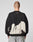 A person with a shaved head faces away wearing the LIVE FAST DIE YOUNG LFDY Mystic Sweater, an oversized black cotton sweatshirt with a white abstract back pattern, topstitching, small white neckline text, and paired with light gray jeans.