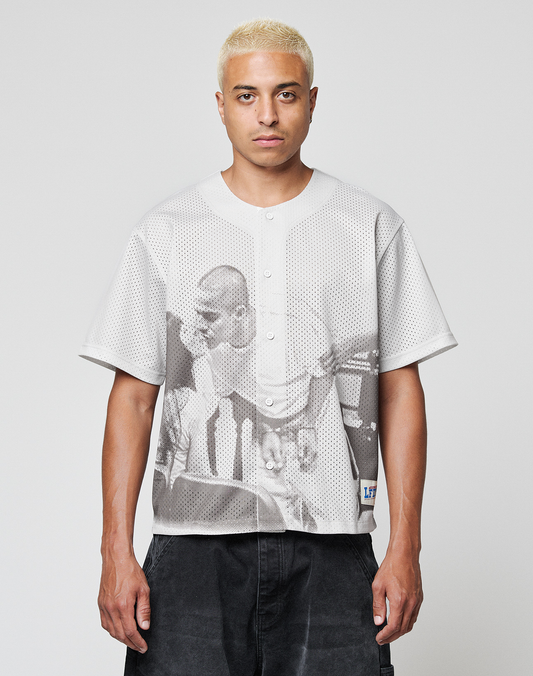 A person with short bleached blond hair wears the LIVE FAST DIE YOUNG LFDY Courtroom Jersey, an oversized light gray mesh button-up featuring a large black-and-white print of two men on the front, standing against a plain light background. | model