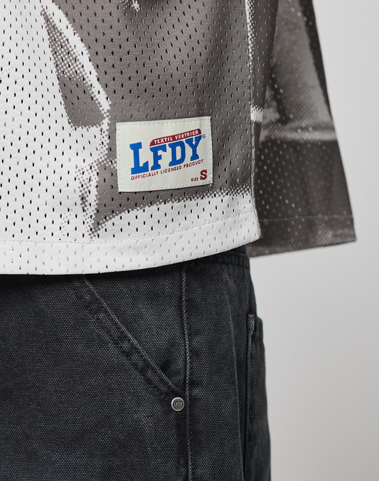 A close-up of the lower part of a person wearing dark pants and the LIVE FAST DIE YOUNG LFDY Courtroom Jersey in size S, featuring a white mesh design, Oversize Fit, LFDY branding, and an Officially Licensed Product patch.