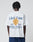 A person wearing the LFDY Paris Tee by LIVE FAST DIE YOUNG, an oversized white cotton T-shirt with blue and yellow front and back graphics reading “Live Fast™ Paris, France” and French text, stands against a plain light background.