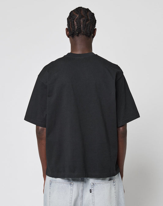 A person with braided hair stands with their back to the camera, wearing a LIVE FAST DIE YOUNG LFDY Triple Racing Tee in black and light-wash denim jeans against a plain white background.