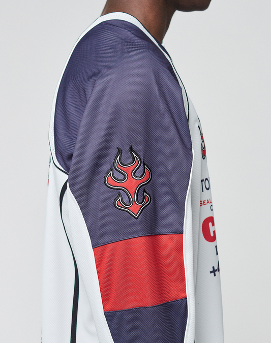 A person in the LIVE FAST DIE YOUNG LFDY Call Us Jersey—an oversize sports top with a flame sleeve logo in purple, white, and red. The side view shows part of the face and highlights the polyester fabric.