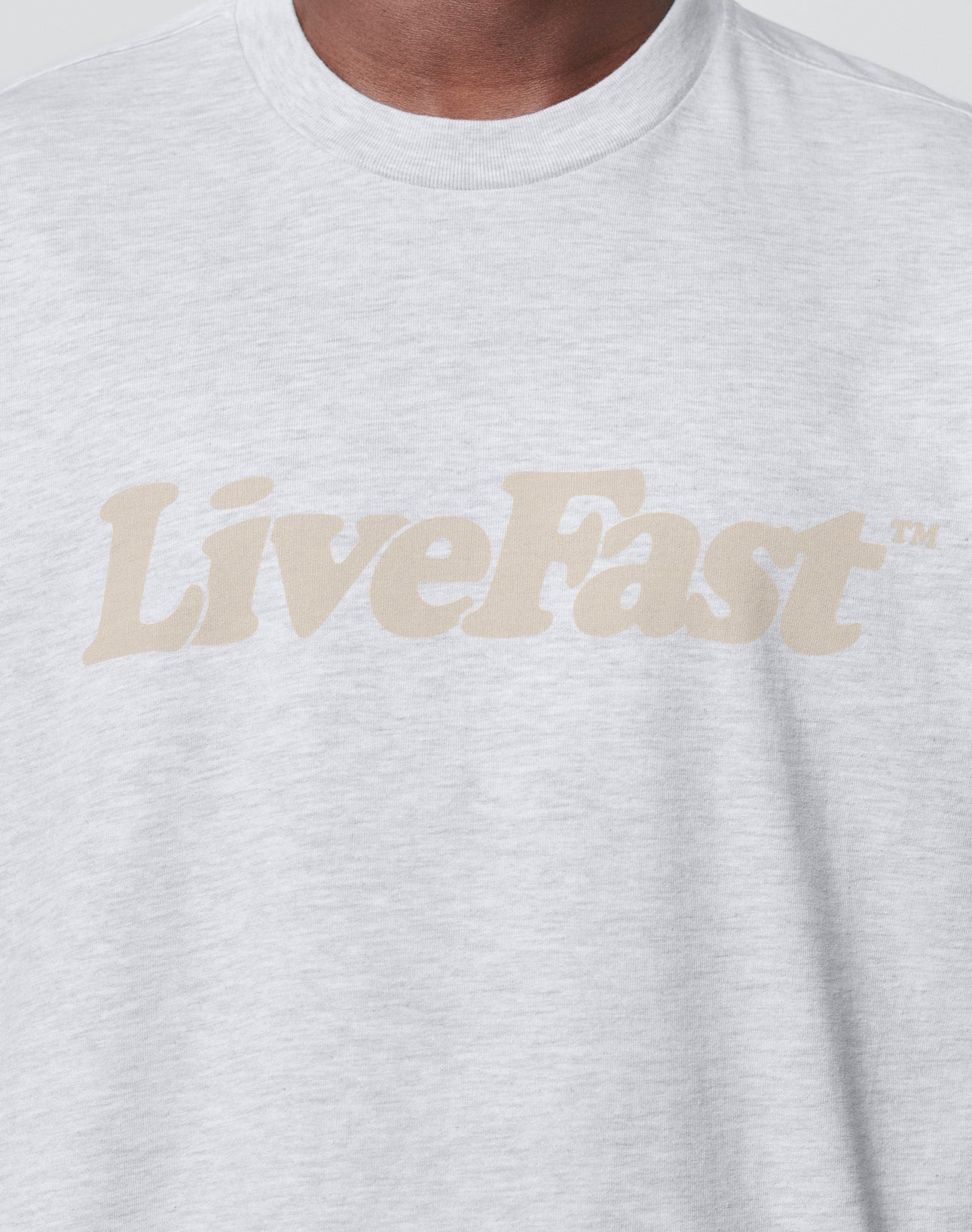 A person wearing a light gray LIVE FAST DIE YOUNG Basic Tee, featuring the brand name printed boldly across the chest.