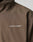 Close-up of the LFDY Trackjacket by LIVE FAST DIE YOUNG, a brown oversized polyester jacket with LIVE FAST in white capitals, a small stylized runner, and reflective print on the left chest.