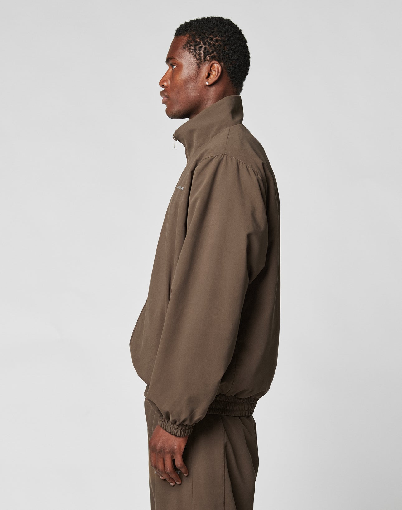 A man in profile wears the LFDY Trackjacket and matching pants by LIVE FAST DIE YOUNG, both in oversized brown polyester, against a light gray background—combining comfort, style, and durability.