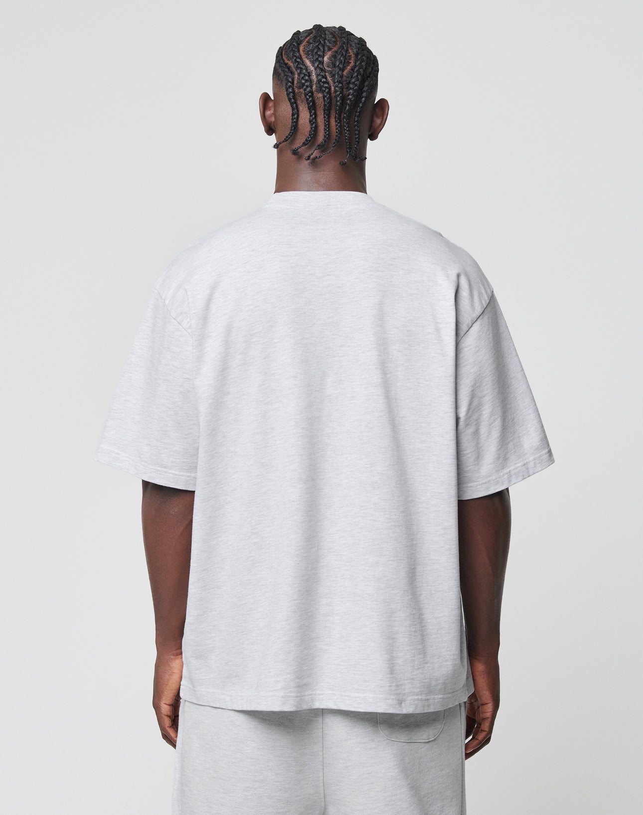 A person with braid-style cornrow hair stands with their back to the camera, wearing the LIVE FAST DIE YOUNG Basic Tee and matching shorts in light gray Baumwolle-Polyester blend, featuring an oversize fit against a plain light background.