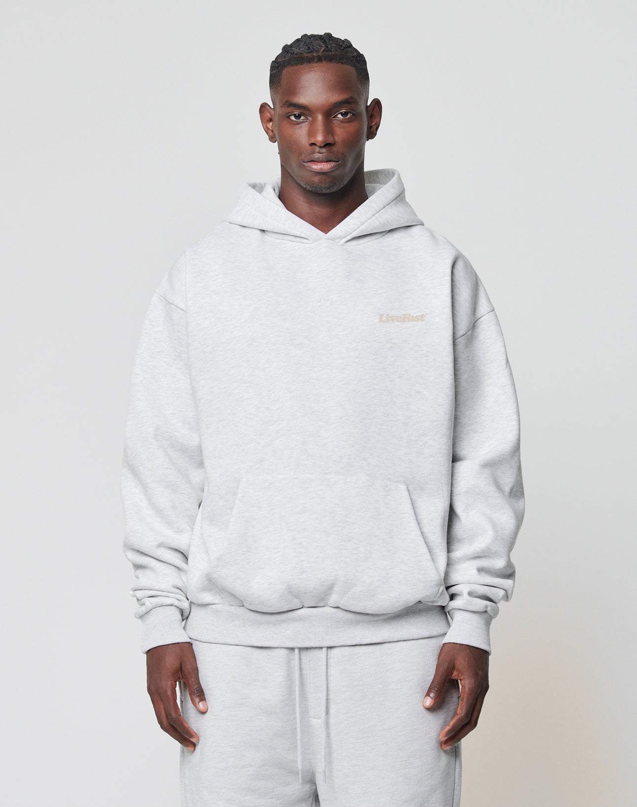 A man faces forward wearing the LIVE FAST DIE YOUNG Basic 360 Hooded sweatshirt in an oversized fit and matching sweatpants, both in light gray Baumwolle, set against a plain light background.