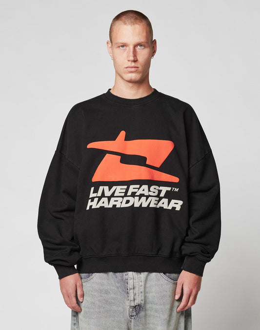 A person with a shaved head wears the LFDY Hardwear Sweater by LIVE FAST DIE YOUNG—a black oversized Baumwolle sweatshirt with a large red abstract pufferprint logo and “LIVE FAST HARDWEAR” in bold white letters—against a plain background.