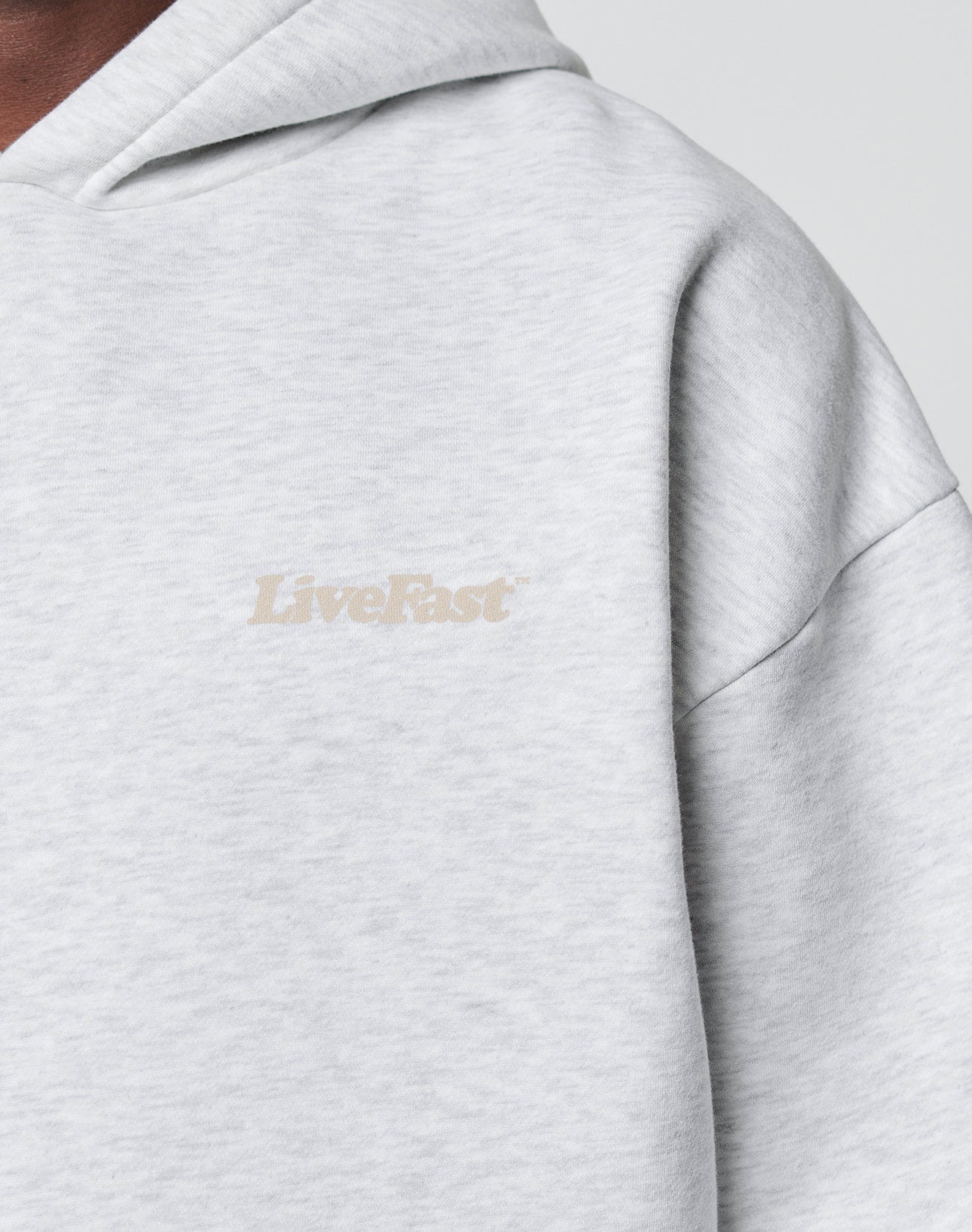 Close-up of the Basic 360 Hooded by LIVE FAST DIE YOUNG, a light gray sweatshirt crafted from soft cotton and polyester, featuring LiveFast in small beige letters on the chest and an Oversize Fit for relaxed comfort.