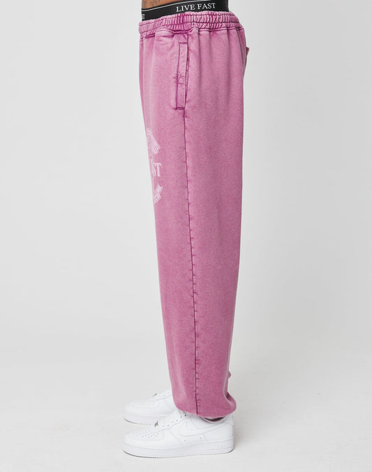 Model wears Loyal Loose Jogger by LIVE FAST DIE YOUNG in pink oversize fit with branded waistband, made from soft Baumwolle. Paired with white sneakers, the model stands sideways against a plain white background.