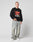 A man with short hair and a neutral expression wears the black LFDY Hardwear Sweater by LIVE FAST DIE YOUNG in Oversize Fit with red and white Pufferprint text, light-washed baggy jeans, and white sneakers. The sweatshirt is made from Baumwolle.